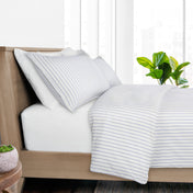 A neatly made bed with white bedding featuring thin blue vertical stripes