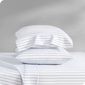 Two pillows with pillowcases on them stacked on a bed