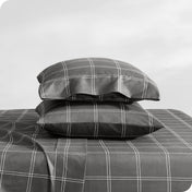 Two pillows with pillowcases on them stacked on a bed