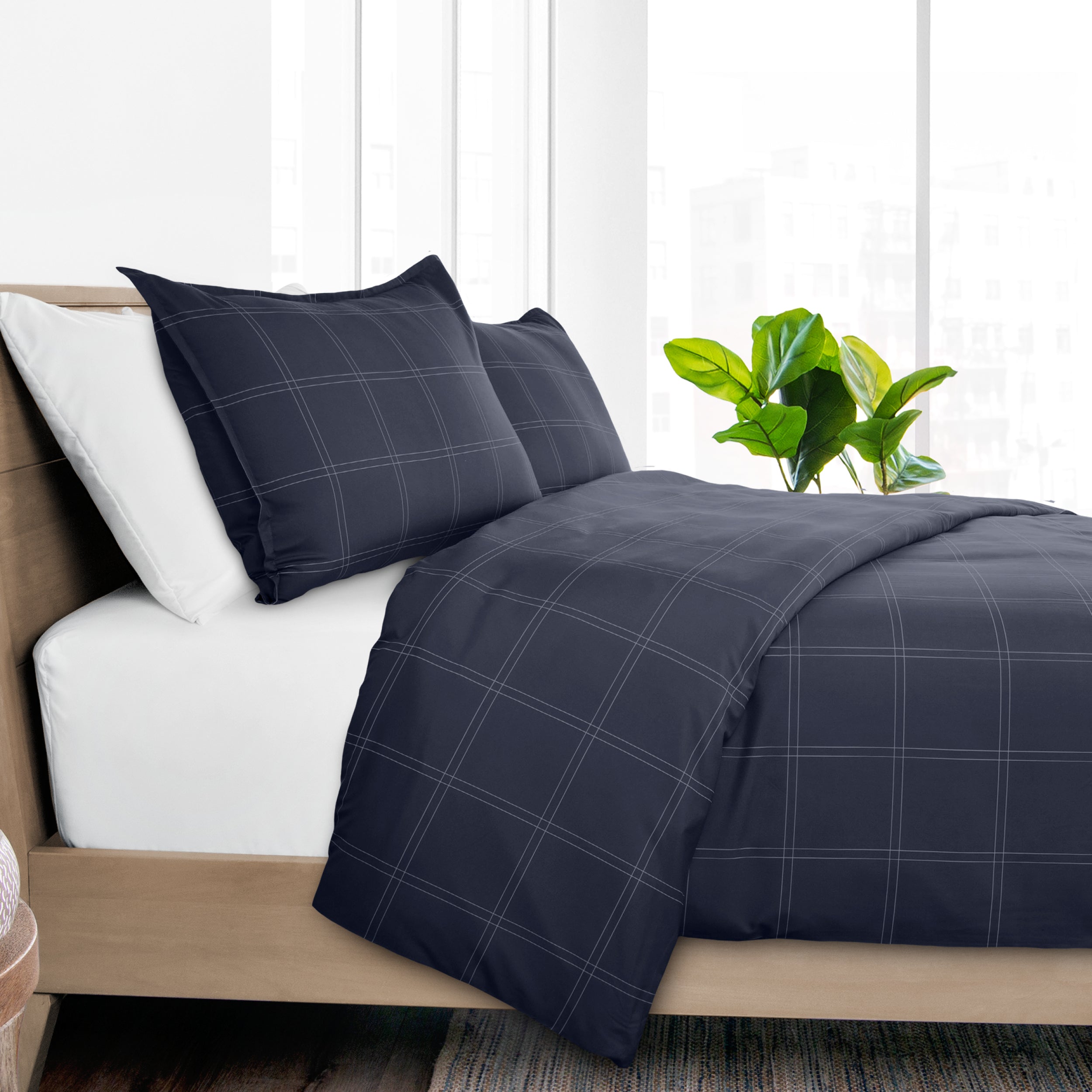 Navy plaid bedding set on a bed with white pillows and a plant in the background.