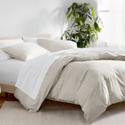 Bed with white and beige bedding in a bright room with a plant.