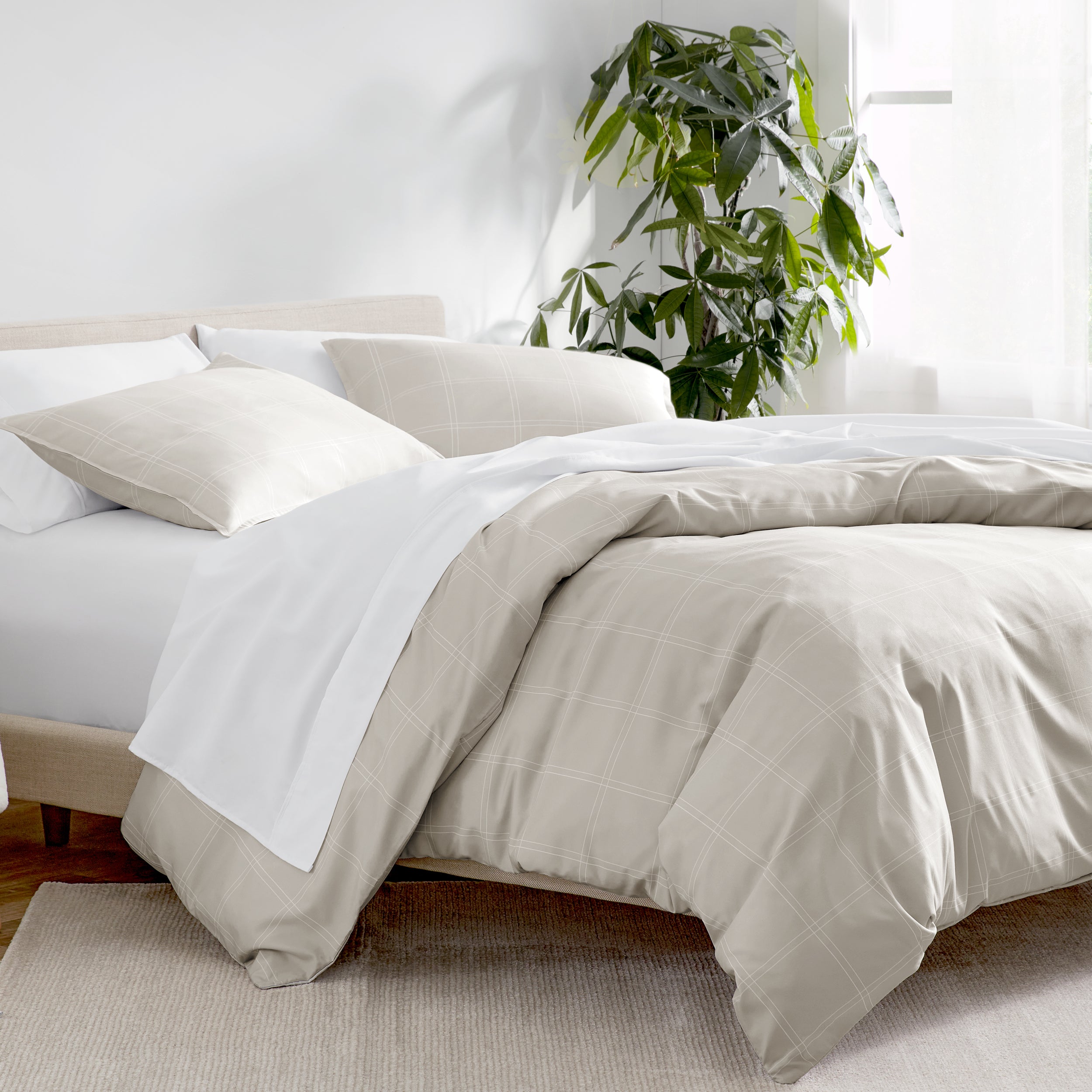 Bed with white and beige bedding in a bright room with a plant.