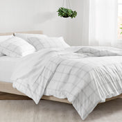 Bed with plaid duvet and white pillows in a bright room.