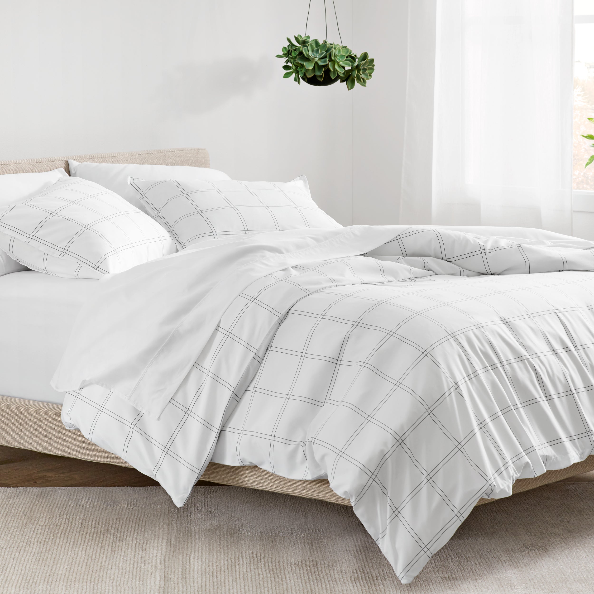 Bed with plaid duvet and white pillows in a bright room.