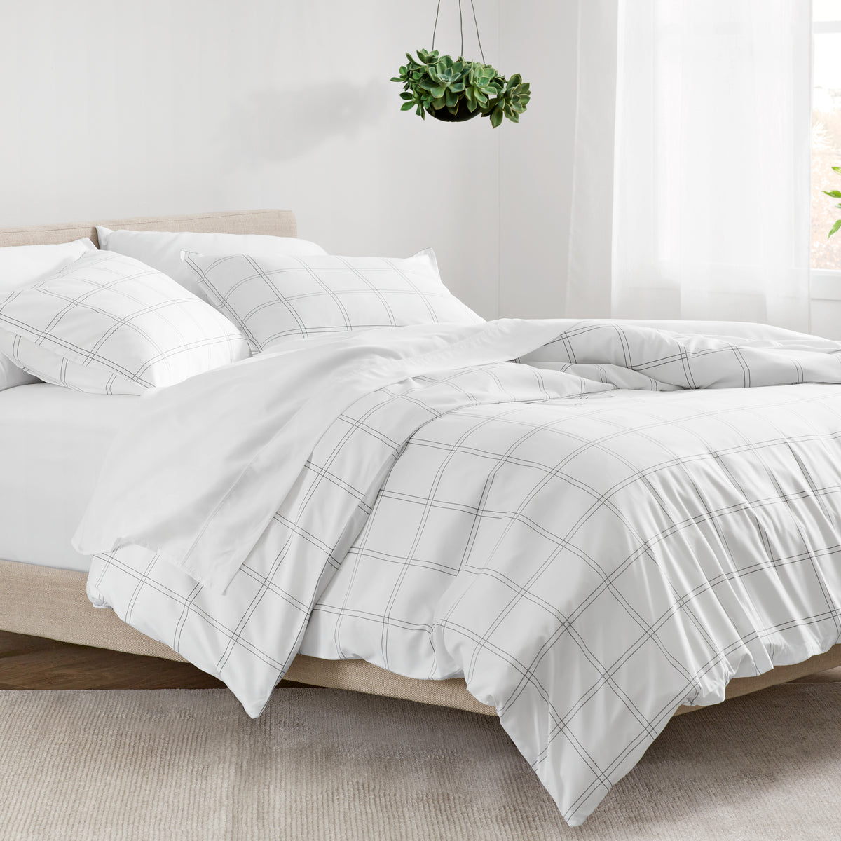 Bed with plaid duvet and white pillows in a bright room.
