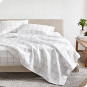 A bed made with plaid sheets where the flat sheet is hanging off the end of the mattress