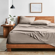 Bedroom with sheet set on a wooden bed frame, side table with plant and lamp.