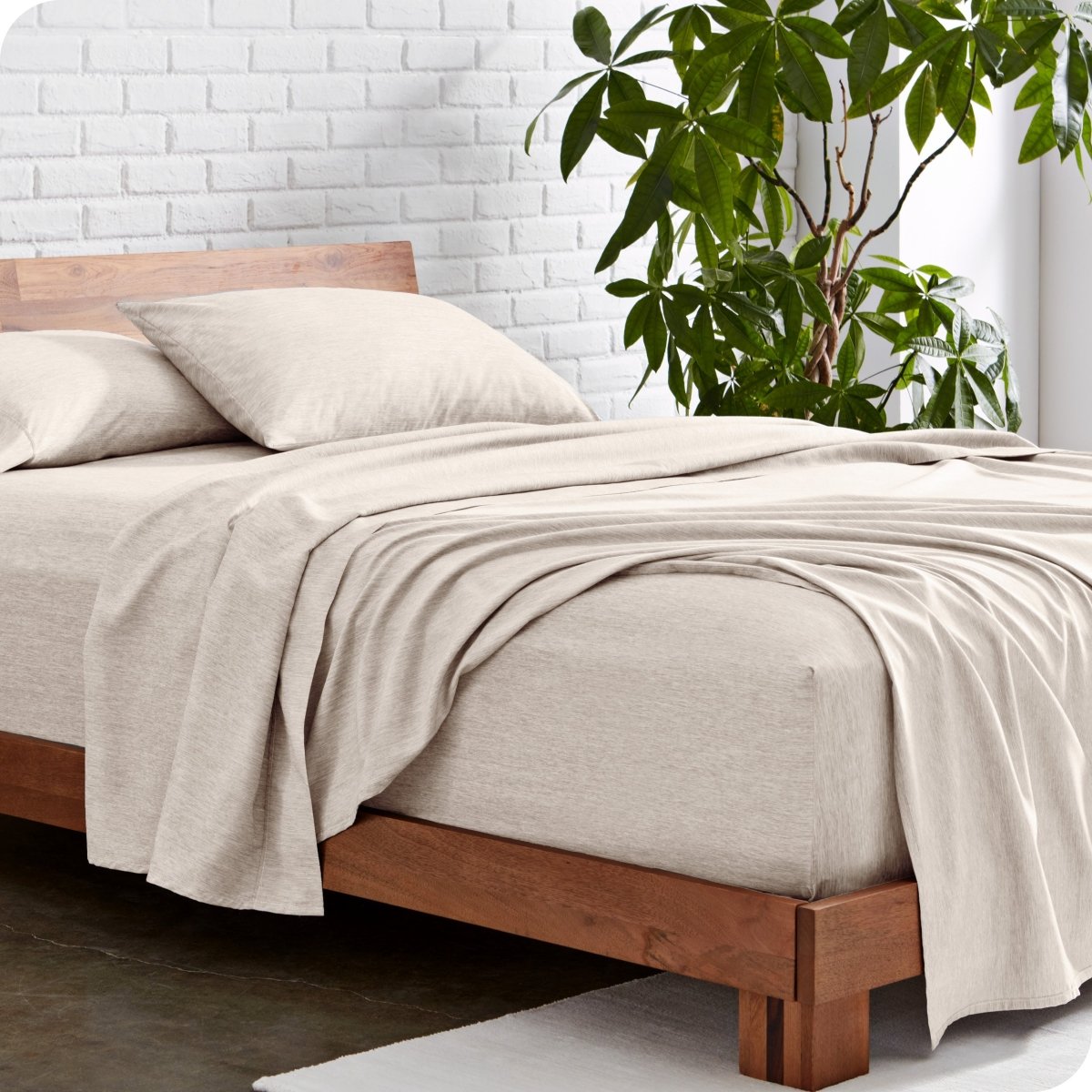 Bed with heather sheets and wooden frame against a white brick wall with a plant.