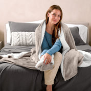 A woman sitting on a bed with a Sherpa blanket around her