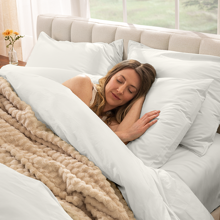 Woman sleeping in a bed with white bedding and beige blanket