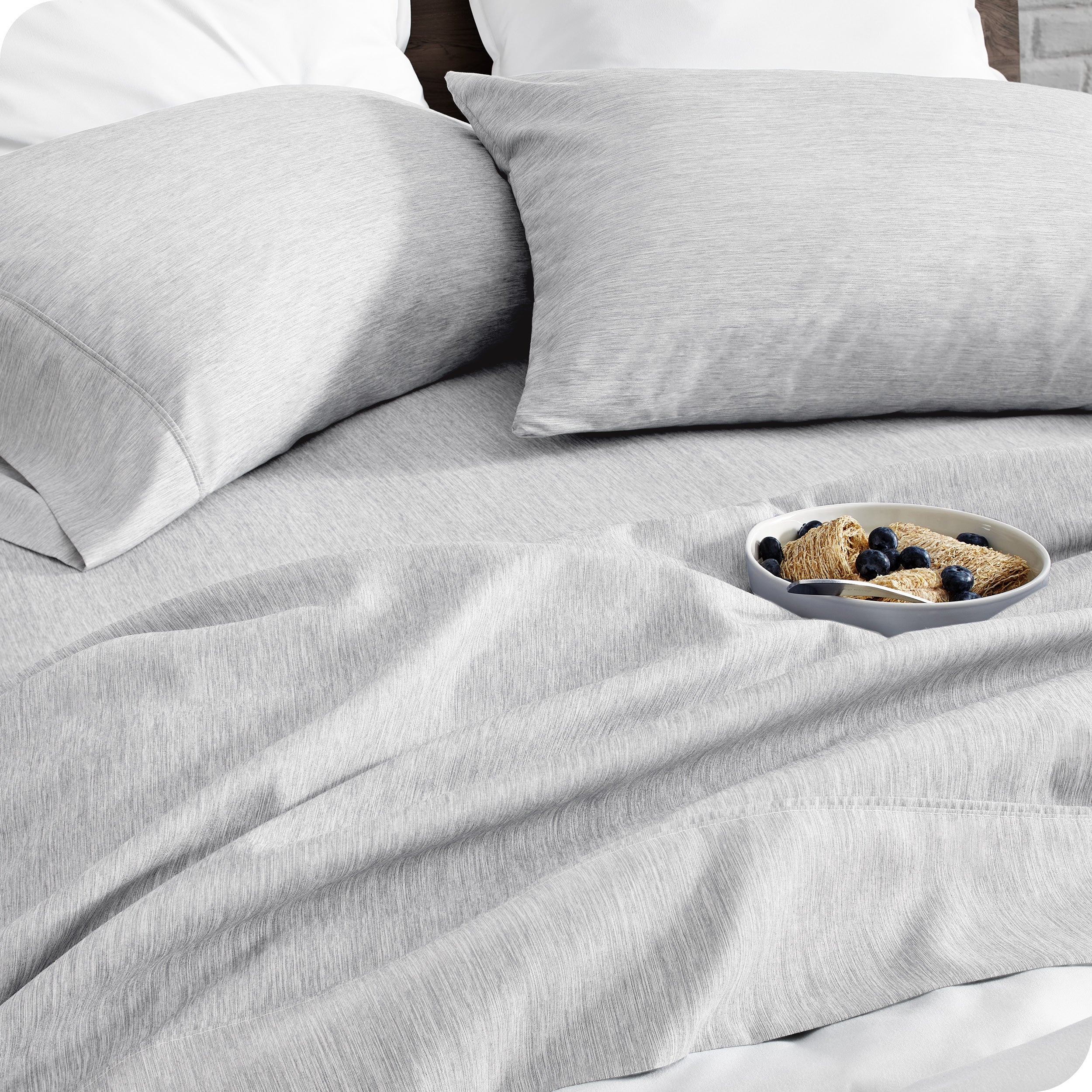 A bed made with sheets. A cereal bowl is on the sheets.