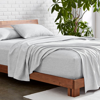Microfiber sheet set on a wooden bed with a plant in the background