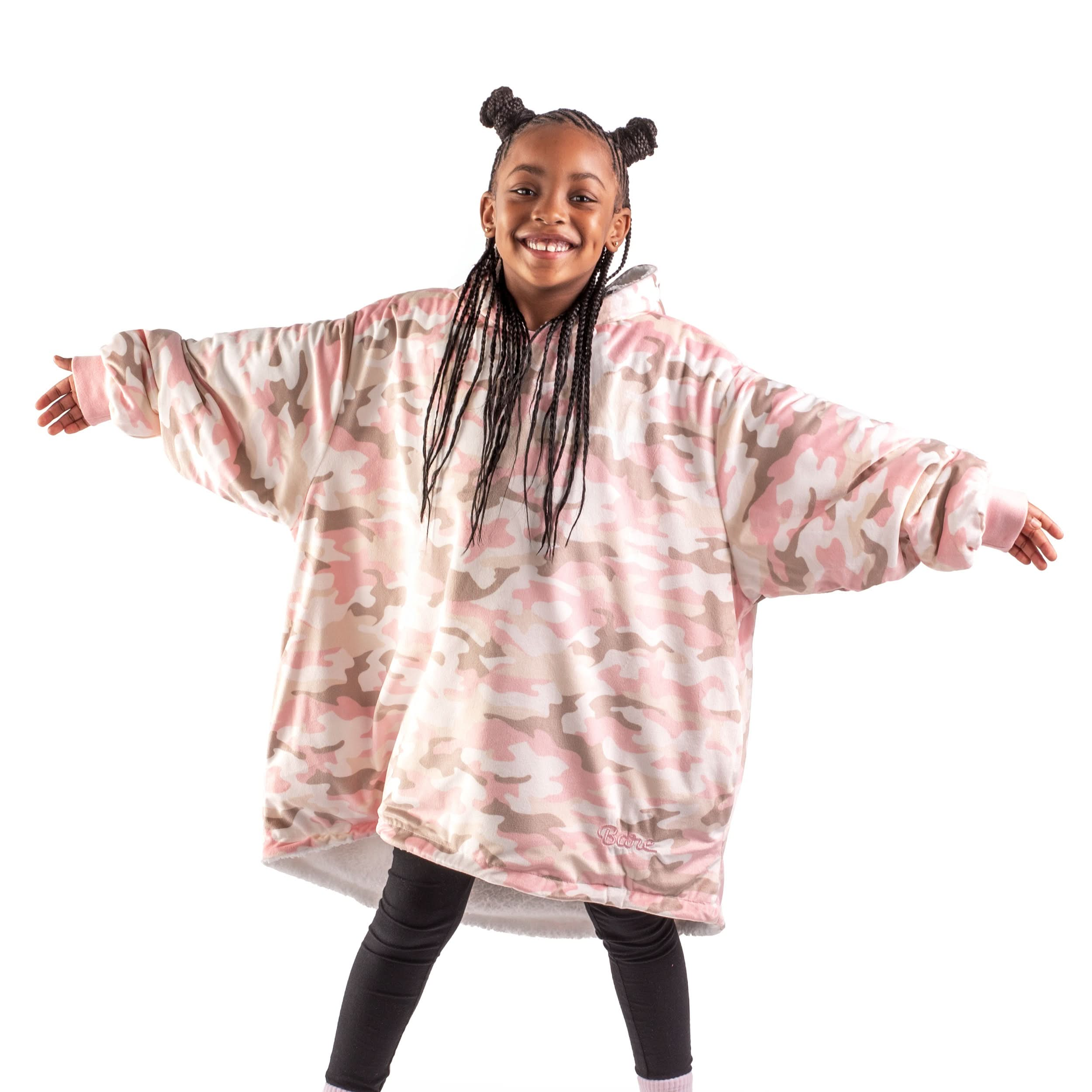 A girl with a wearable blanket on is standing with her arms stretched out