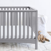 Gray crib with stuffed animals on the floor next to it
