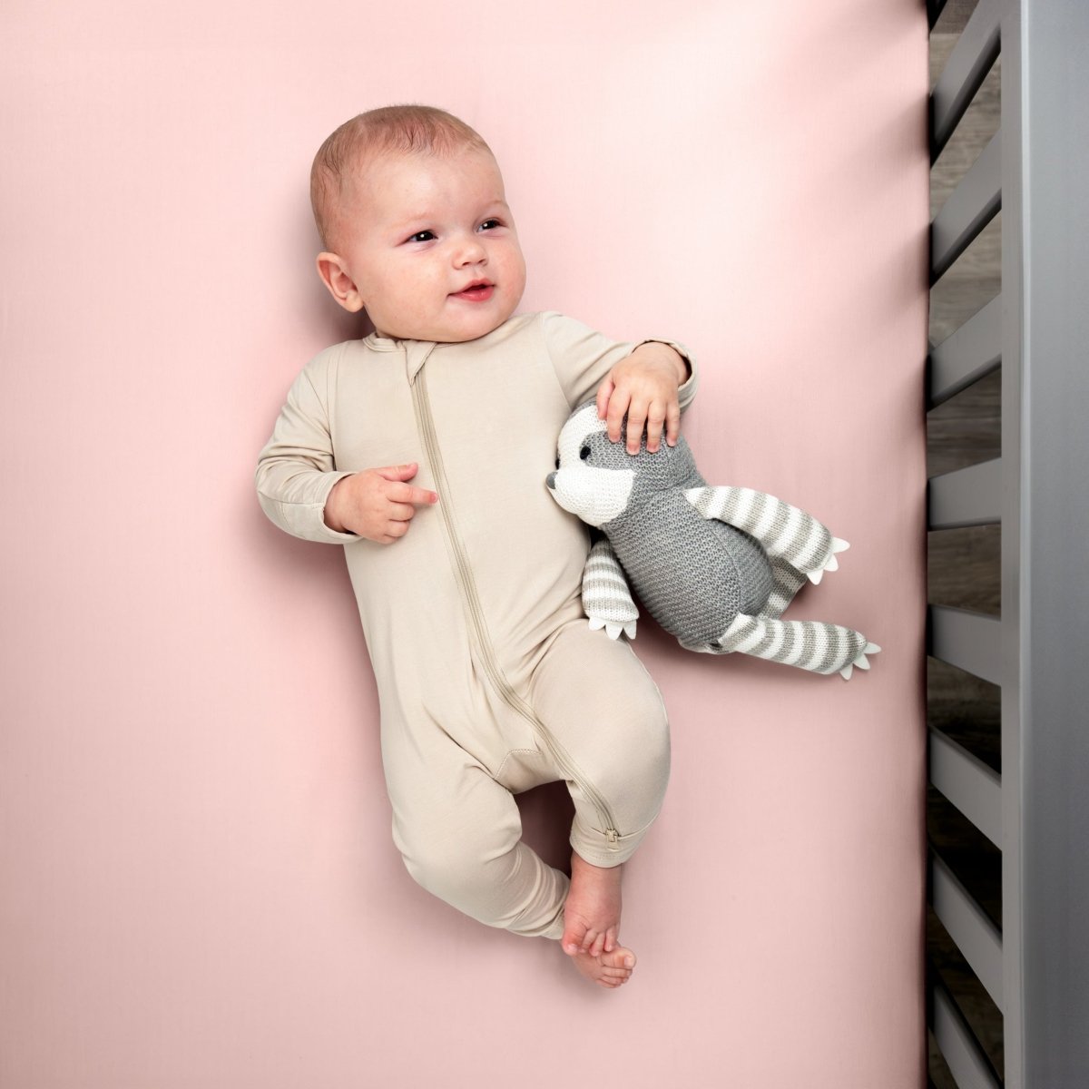 Baby in a beige onesie holding a gray and white striped toy while in a crib