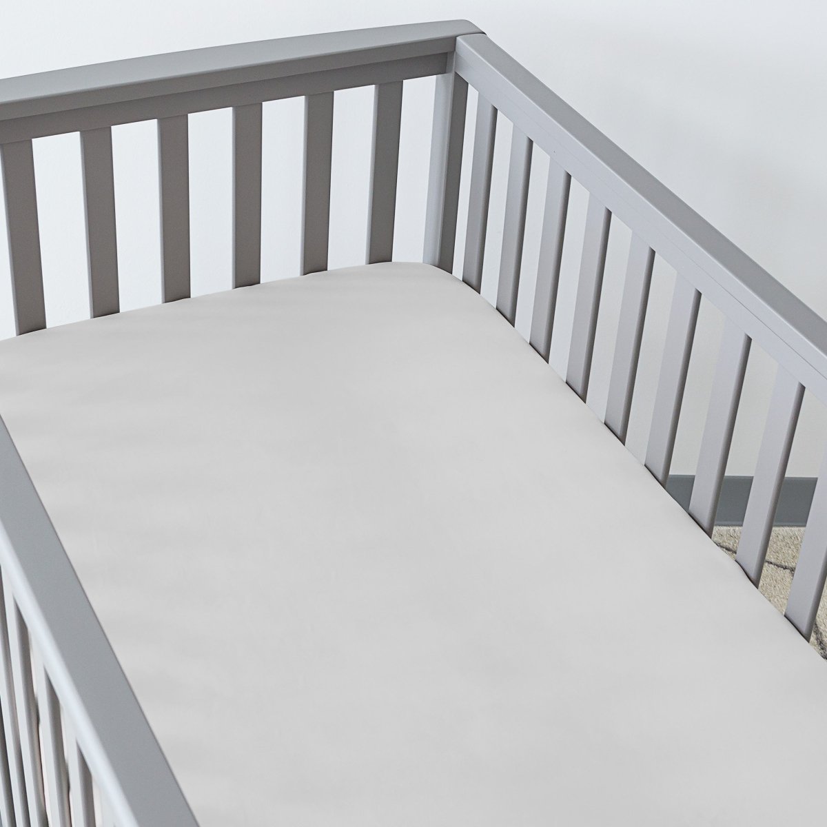 Gray crib with a fitted sheet on the mattress