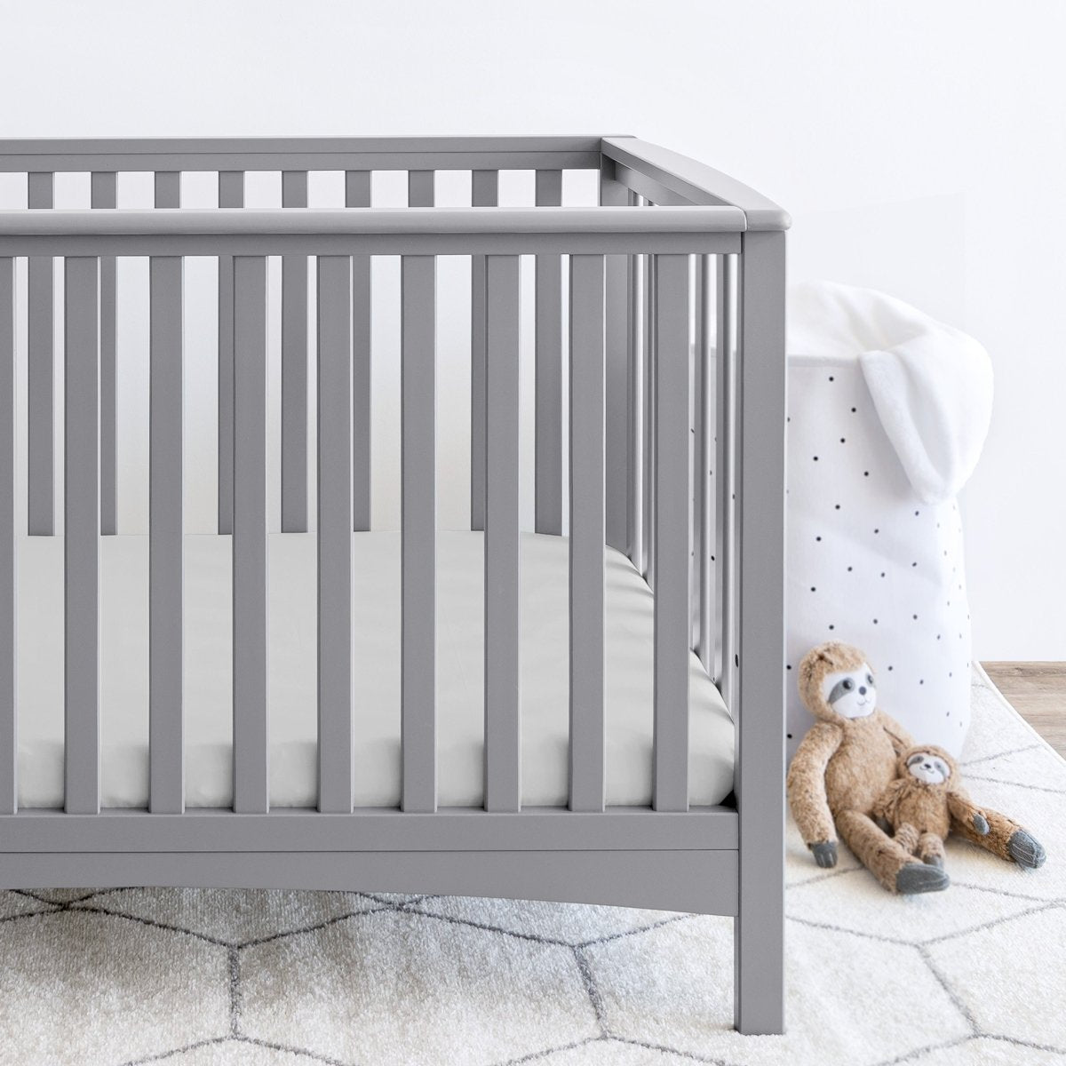 Gray crib with stuffed animals on the floor next to it