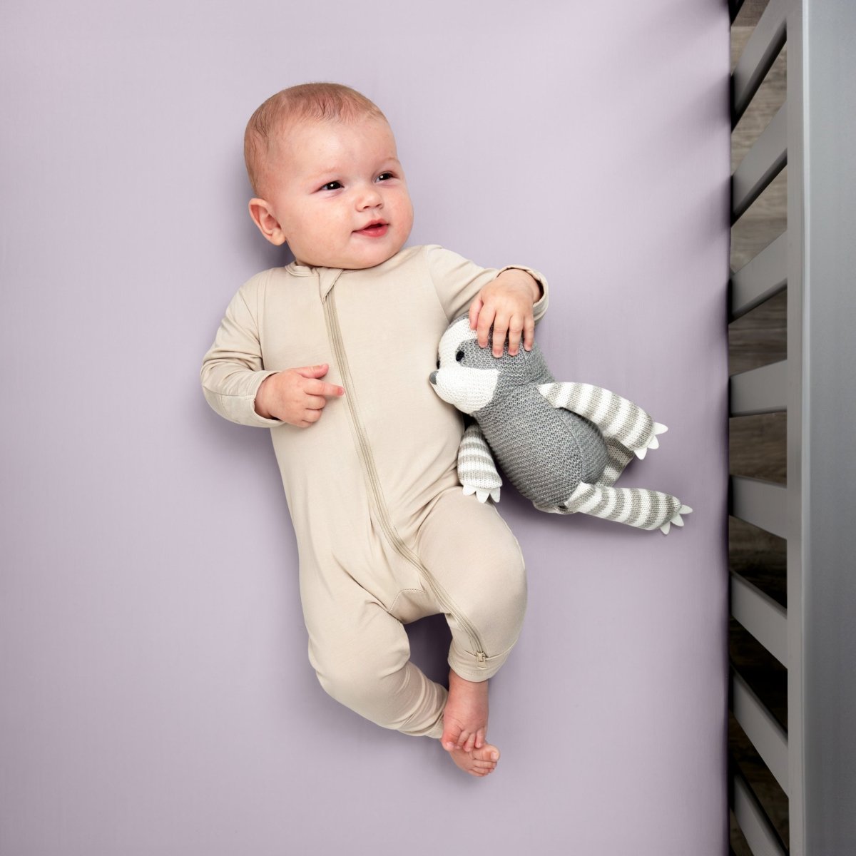 Baby in a beige onesie holding a gray and white striped toy while in a crib