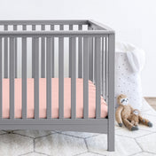 Gray crib with stuffed animals on the floor next to it