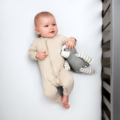 Baby in a beige onesie holding a gray and white striped toy while in a crib