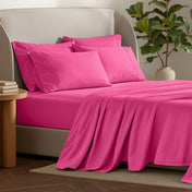 Bed sheets and pillows on a bed with a plant and side table in the background.