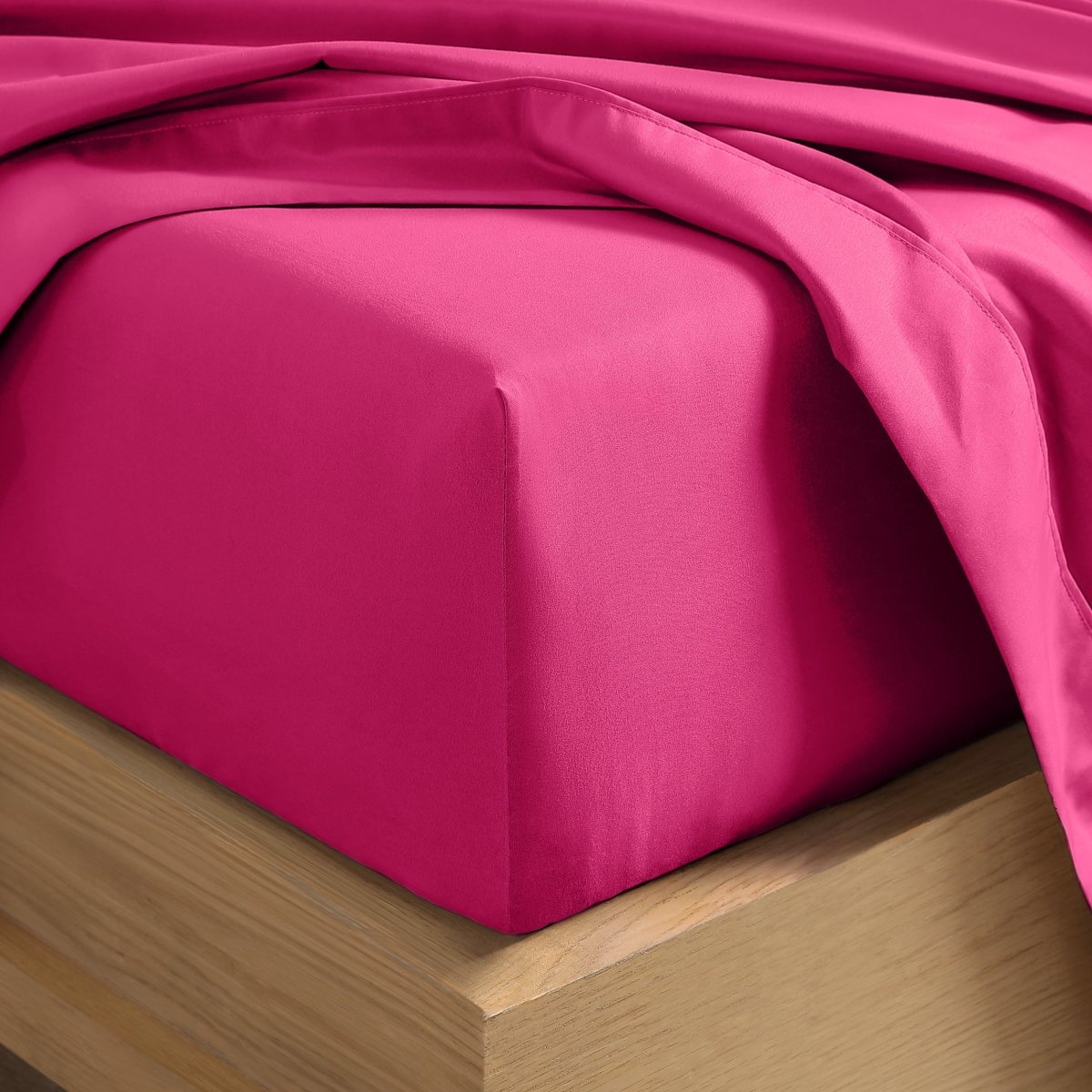 A close-up of a fitted sheet covering the corner of a bed frame, with matching top sheet draped over it.