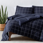 Navy blue plaid comforter set on a bed with a plant in the corner.