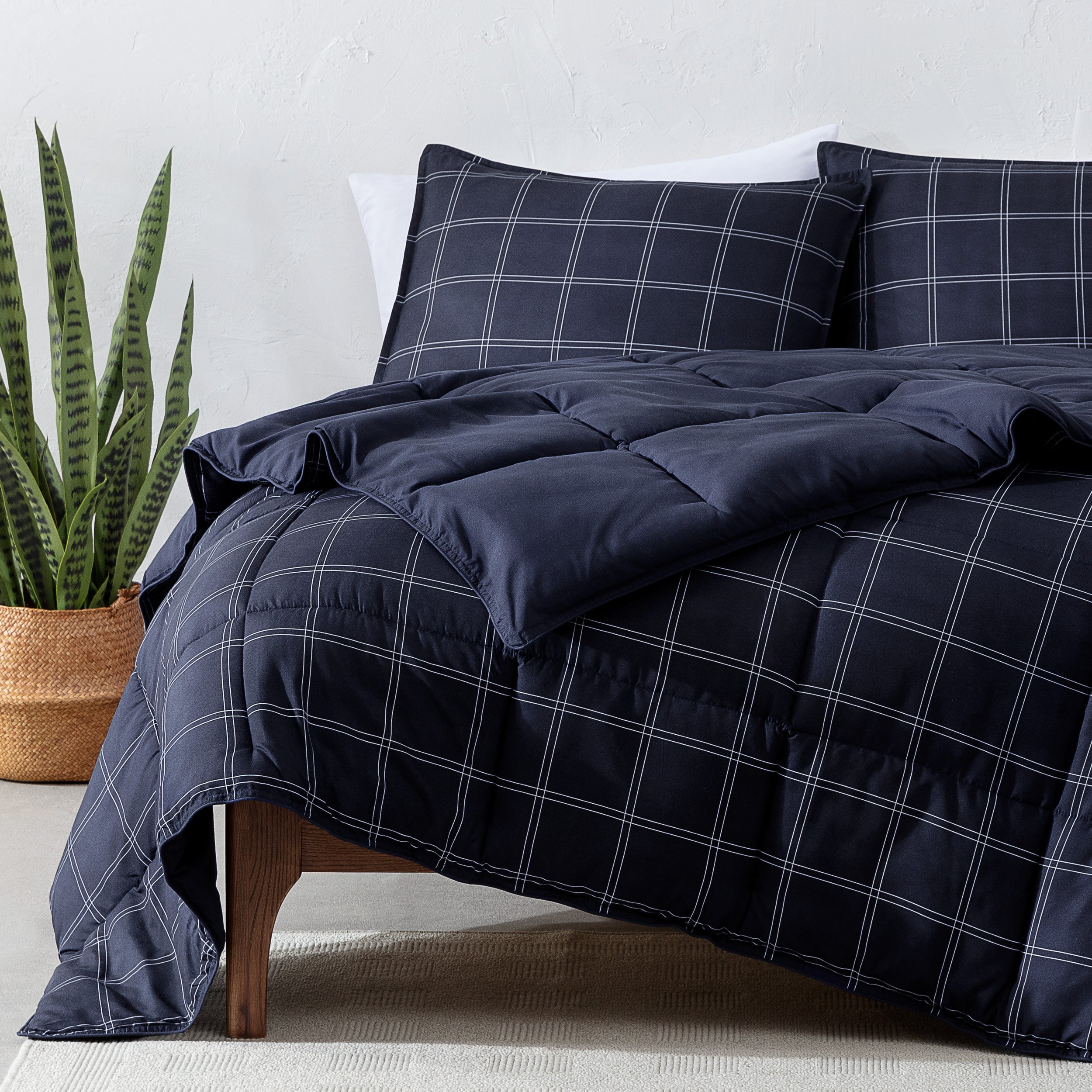 Navy blue plaid comforter set on a bed with a plant in the corner.
