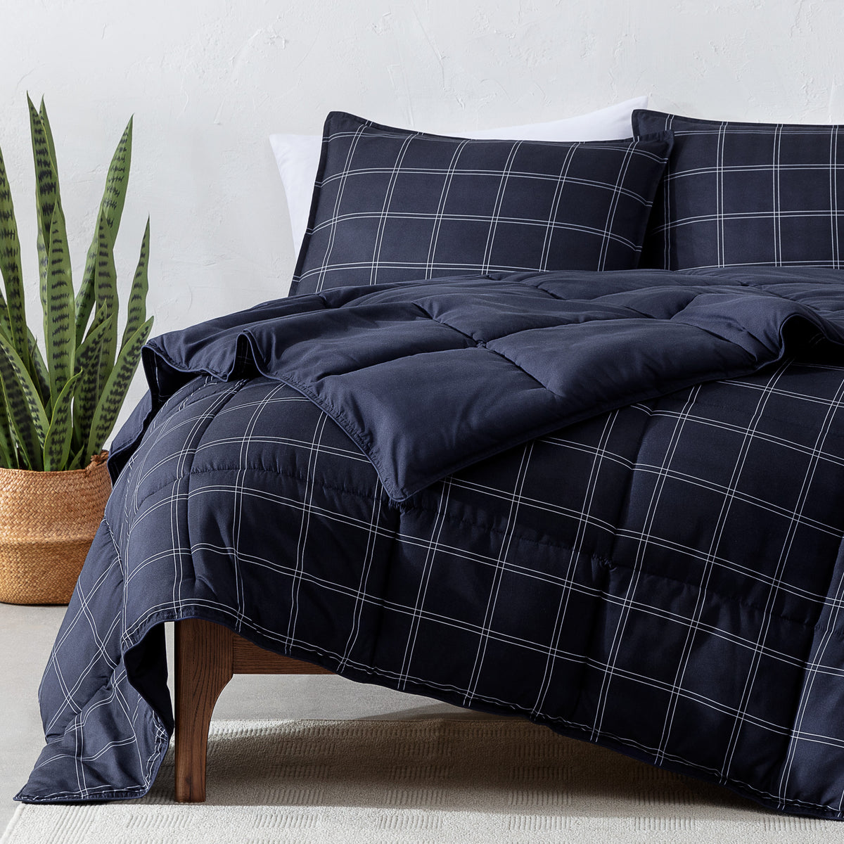 Navy blue plaid comforter set on a bed with a plant in the corner.
