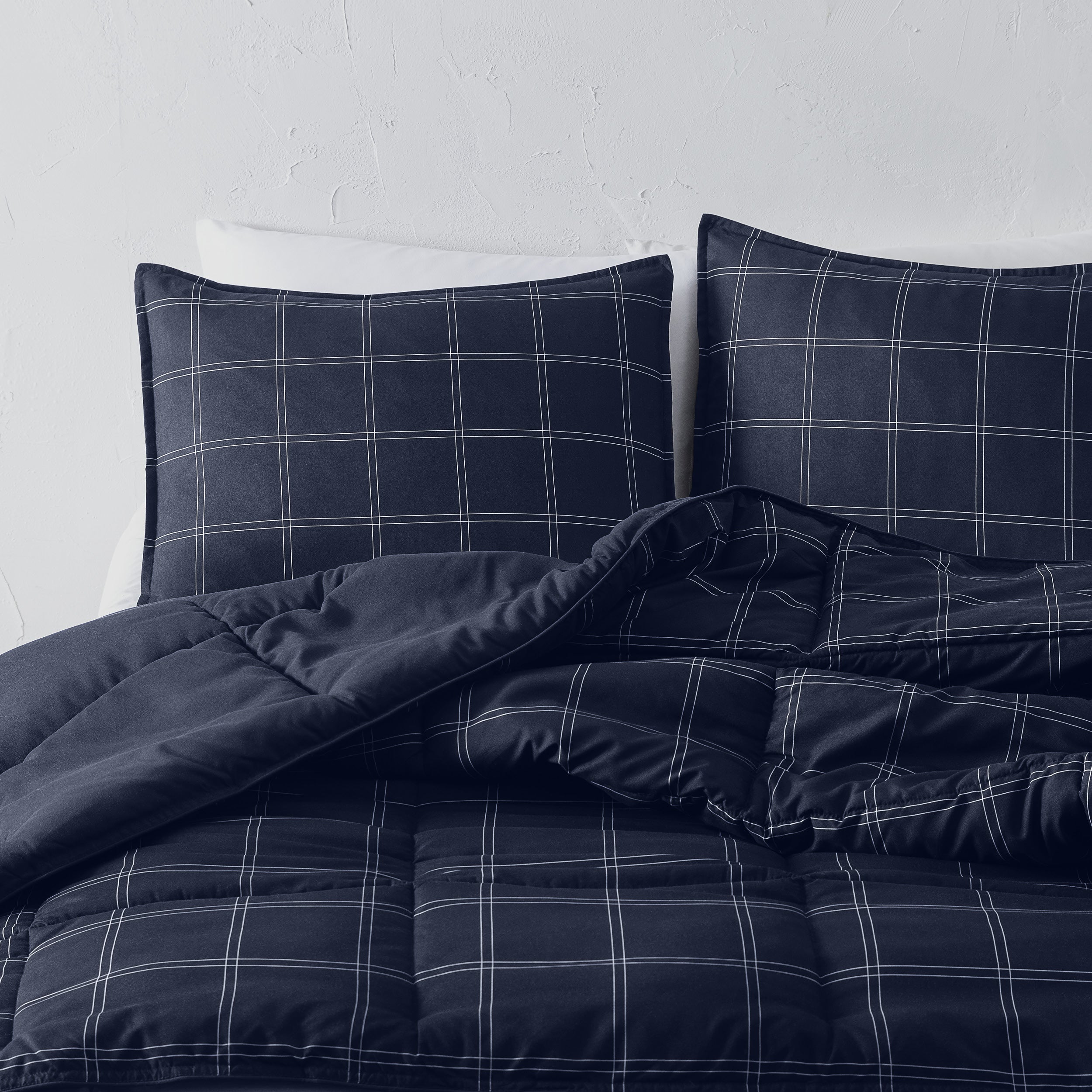 Navy blue plaid bedding set on a bed with a white wall background