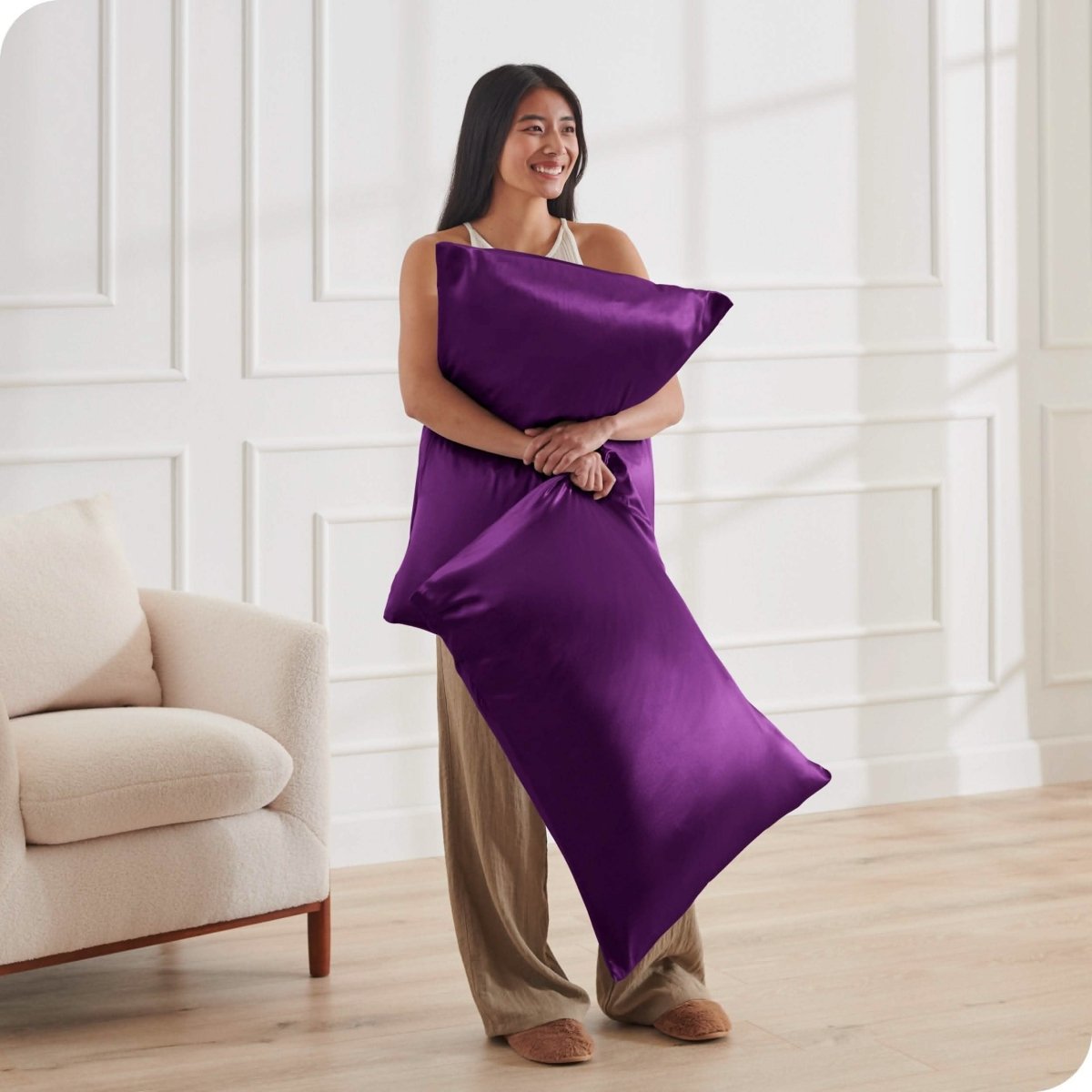 A woman standing while holding pillows with silk pillowcases on them