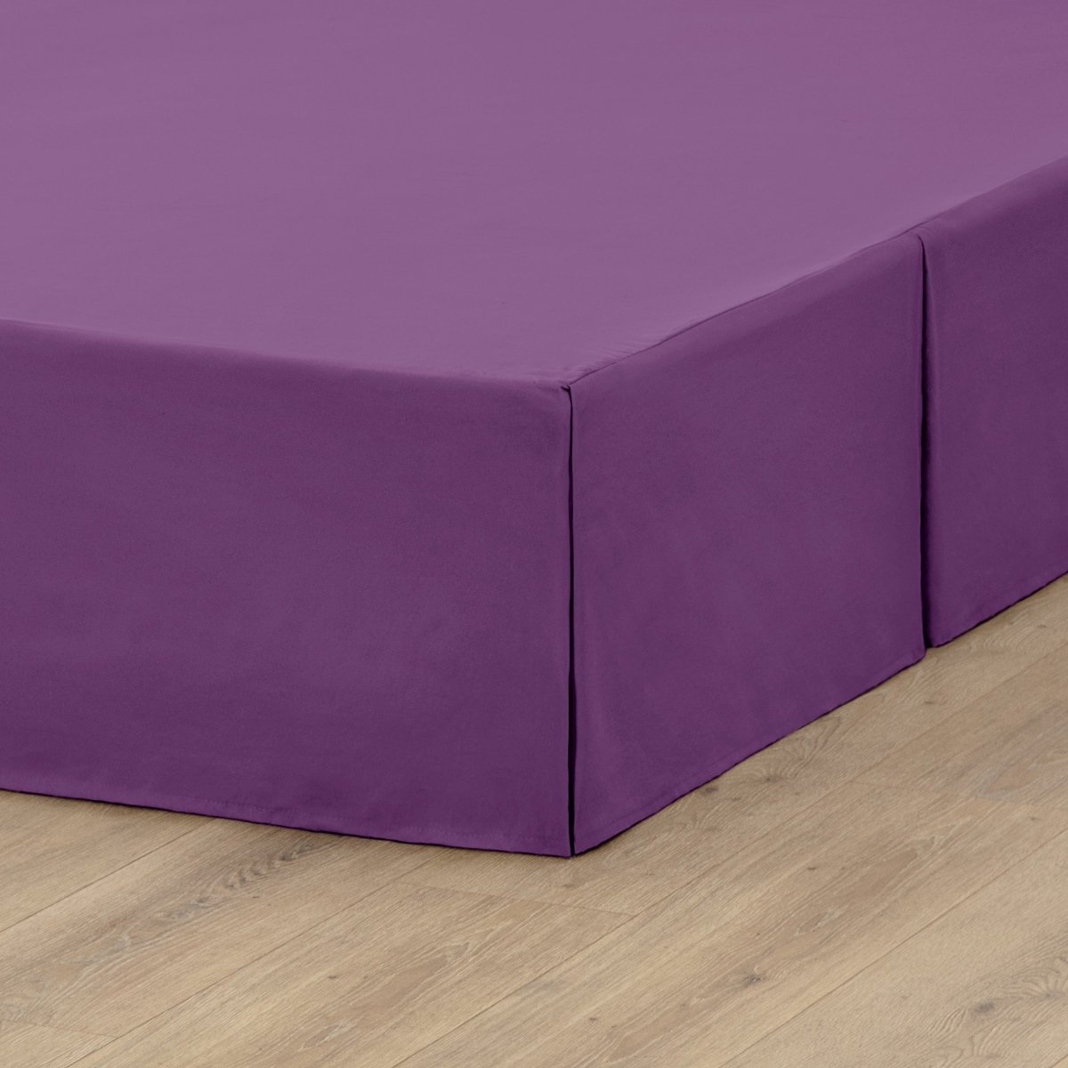 The corner of a box spring with a pleated bed skirt on it