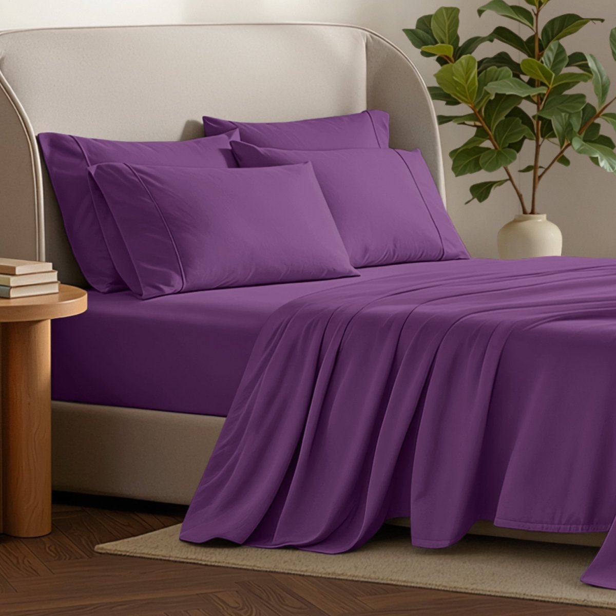 Bed sheets and pillows on a bed with a plant and side table in the background.