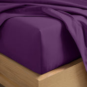 A close-up of a fitted sheet covering the corner of a bed frame, with matching top sheet draped over it.