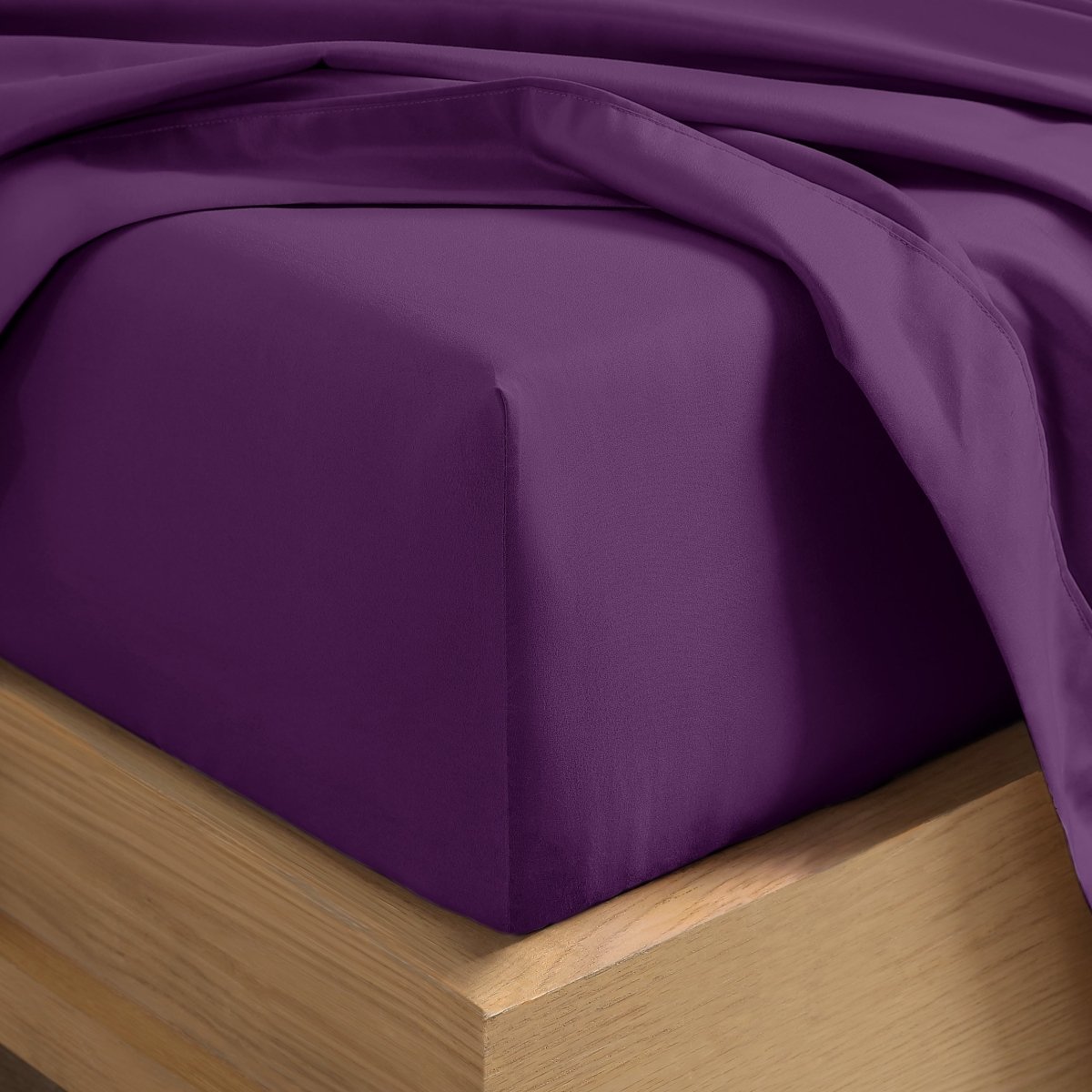 A close-up of a fitted sheet covering the corner of a bed frame, with matching top sheet draped over it.