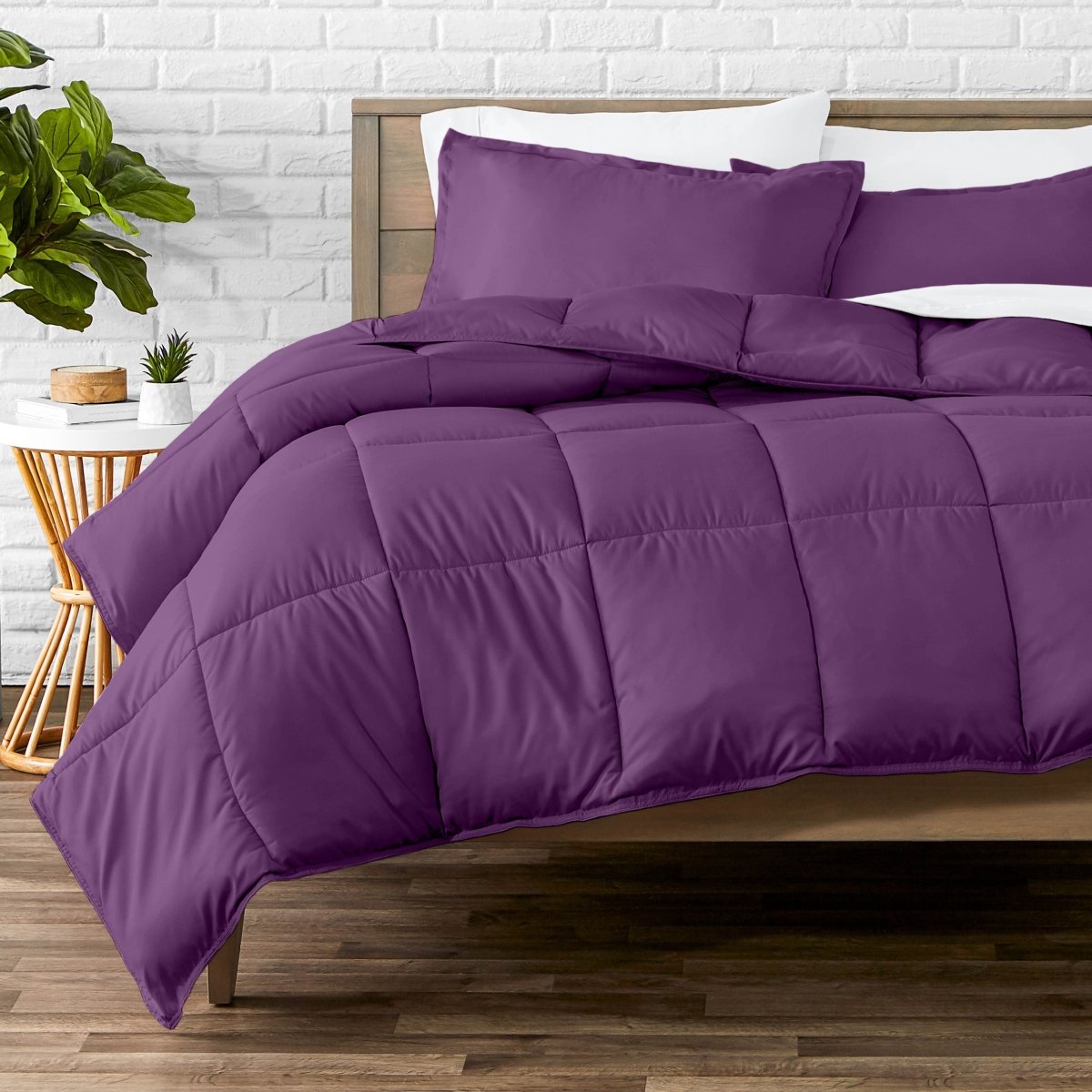 Comforter set on a bed with a white brick wall and plant in the background