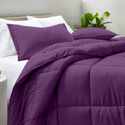 Comforter and pillow shams on a bed with a white brick wall and plant in the background