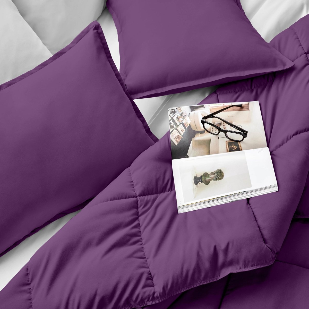 Comforter and pillows on a bed with a magazine and glasses.
