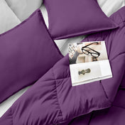 Comforter and pillows on a bed with a magazine and glasses.