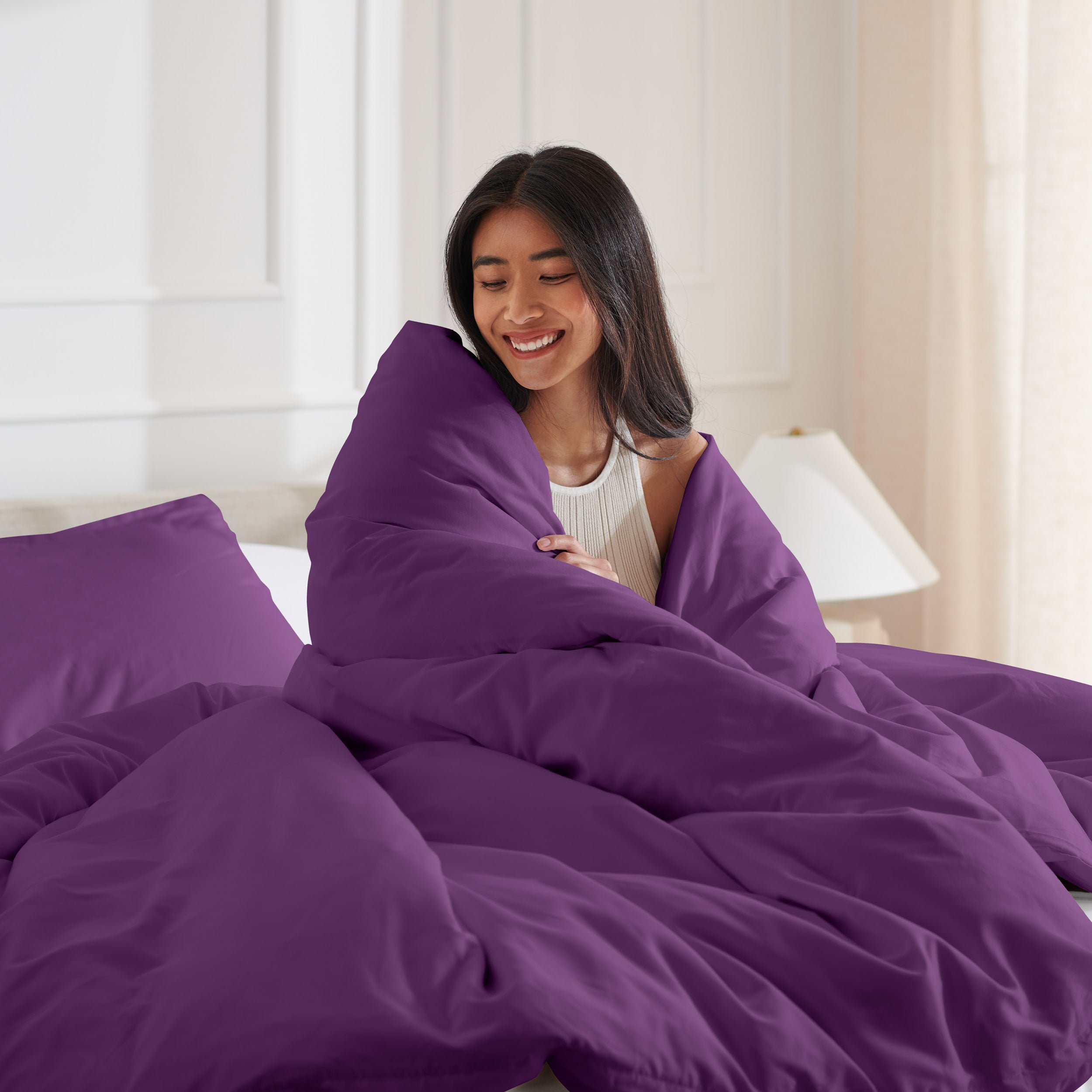 Woman smiling under duvet cover set in a bedroom setting