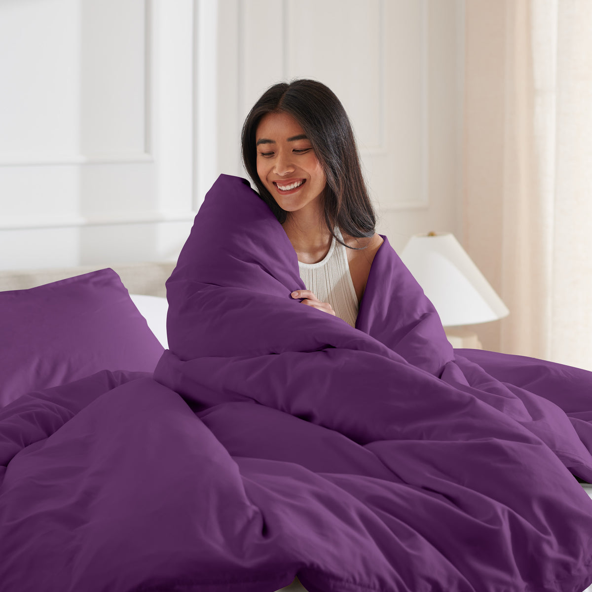Woman smiling under duvet cover set in a bedroom setting
