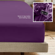 A fitted bed sheet on a bed frame with a small inset close-up of the elastic and a sewn-in tag labeled BOTTOM. White text on the sheet reads, 'Sewn-in tag makes bed-making easy.