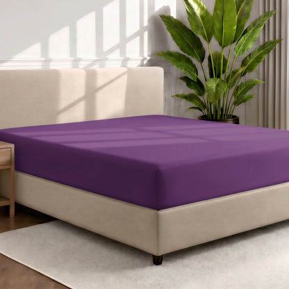 Bed with a fitted sheet in a room with a large plant and rug