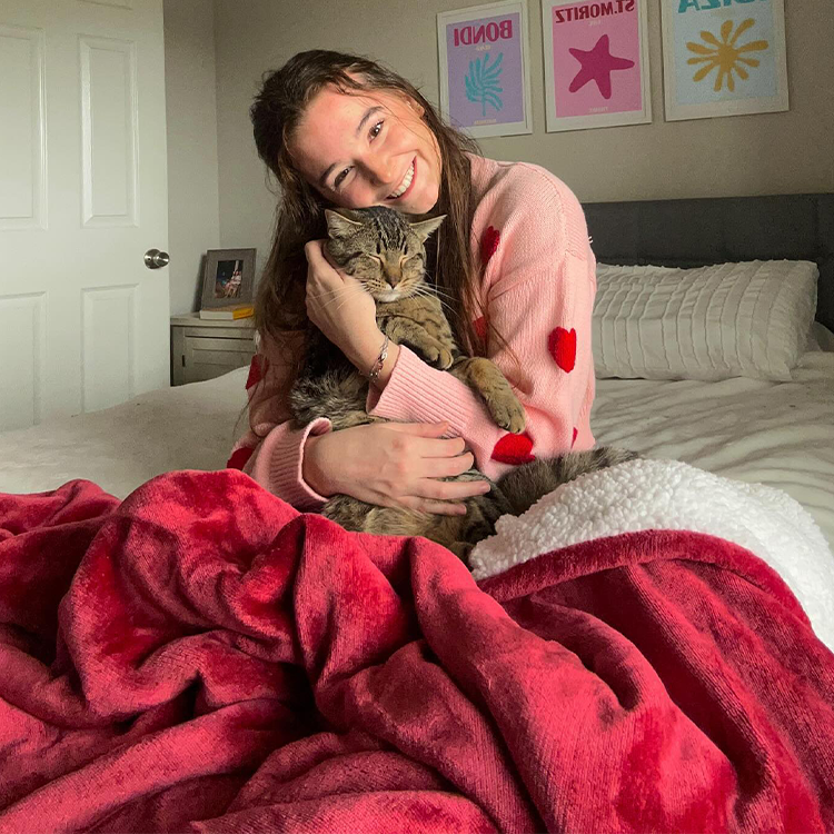 Woman in a pink robe holding a cat on a bed with a red blanket