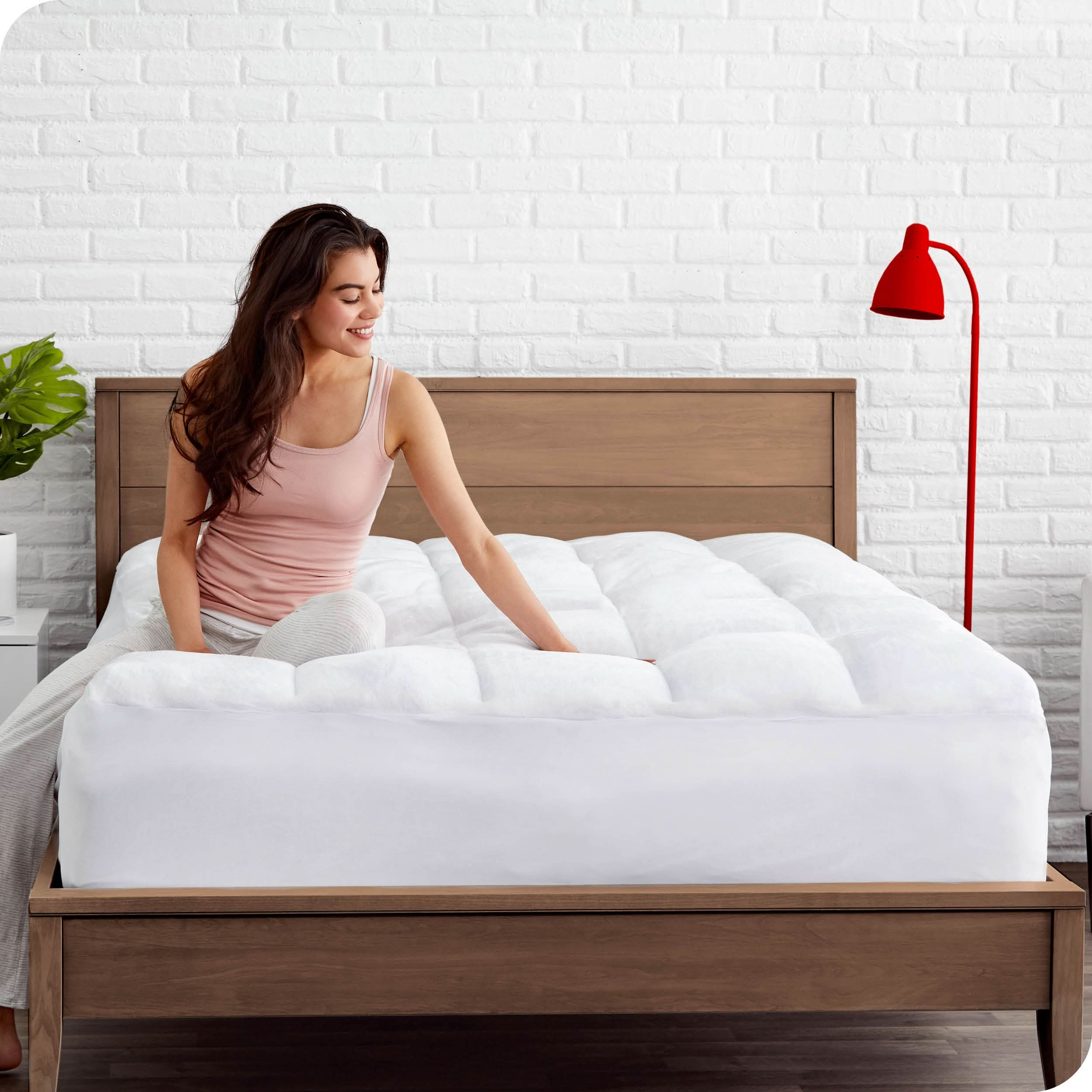 A woman is sitting on a mattress which has a white mattress pad on it.