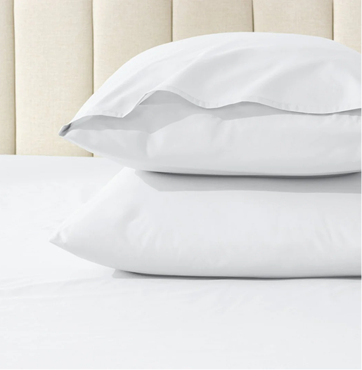 Two white pillows on a bed with a beige headboard.