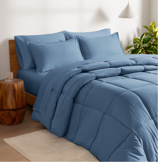 Blue bedding set on a bed in a bedroom with a wooden side table and plant.
