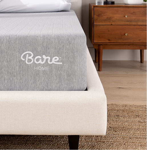 Gray mattress with Bare Home logo on a bed frame, next to a wooden nightstand.