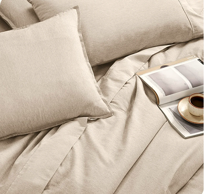 Bed made with a beige sheet set and a folded pillowcase on top