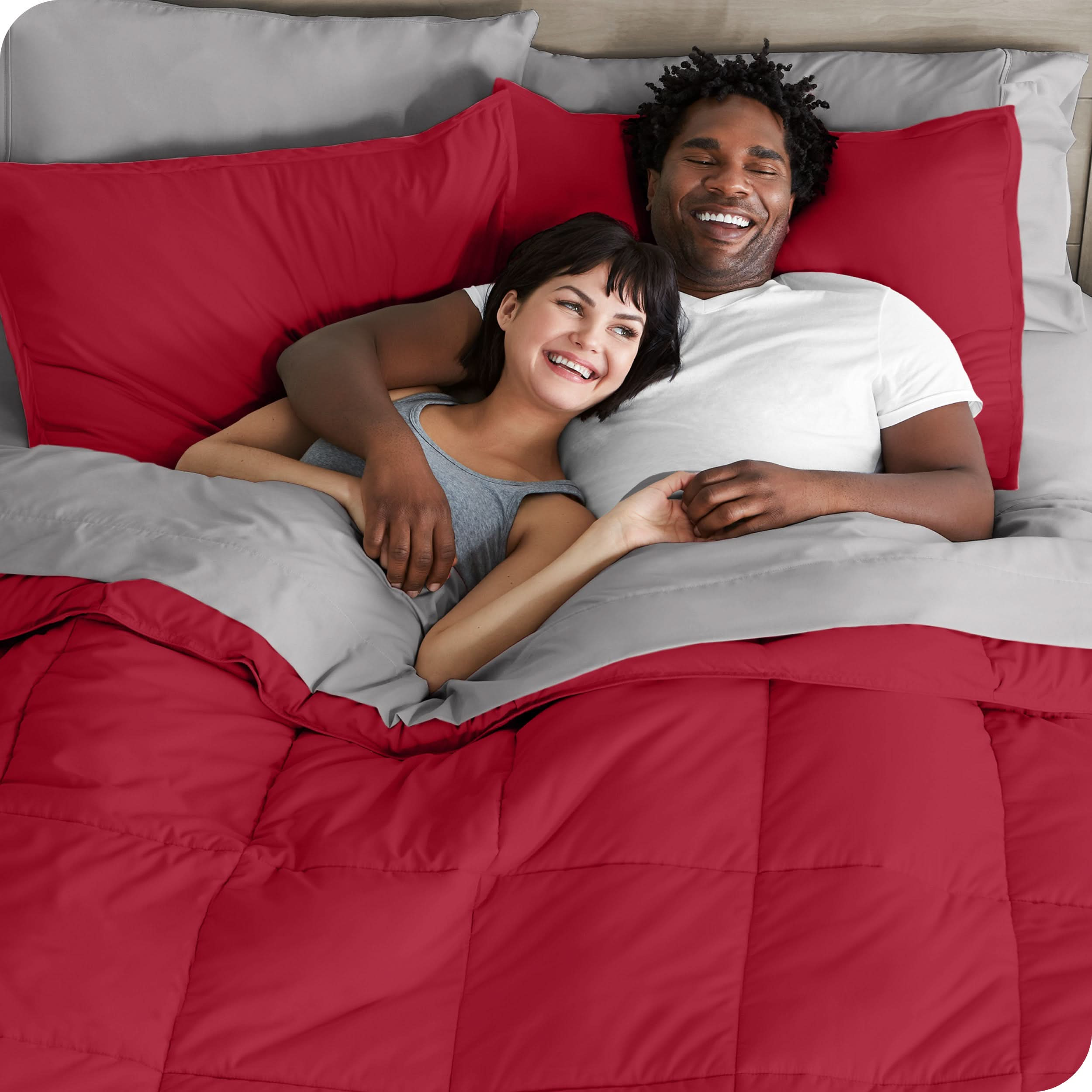 A couple is lying in bed with a comforter and sheets over them